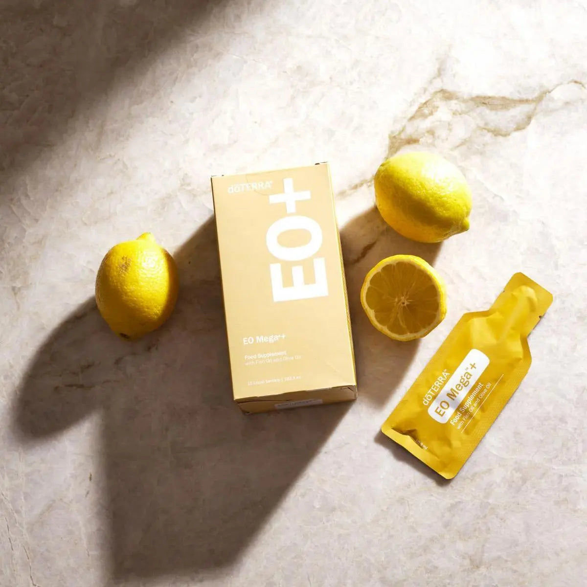 Caja y sobre de EO Mega+ dōTERRA con limones sobre mármol visto desde arriba con sombras