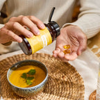 Manos sosteniendo frasco de Cápsulas EO Mega+ dōTERRA con softgels en cuenco de sopa