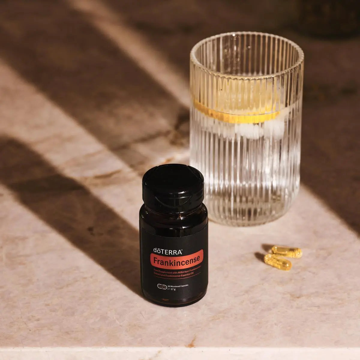 Frasco de Cápsulas de Incienso dōTERRA con vaso de agua y limón sobre mármol