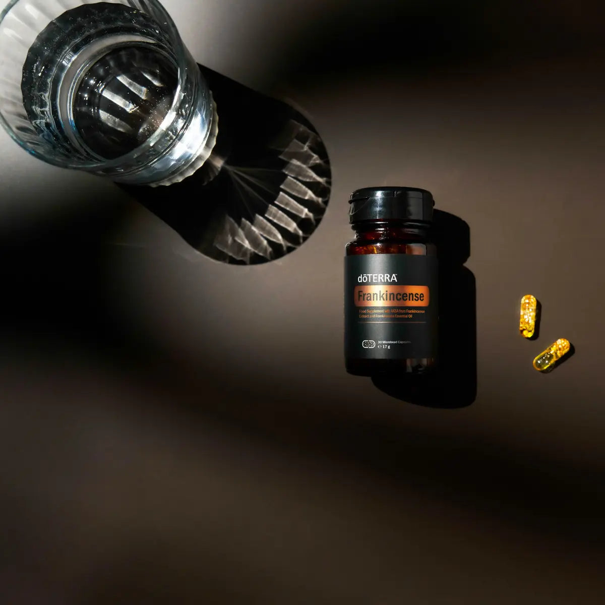 Frasco de Cápsulas de Incienso dōTERRA con vaso de cristal sobre fondo oscuro visto desde arriba