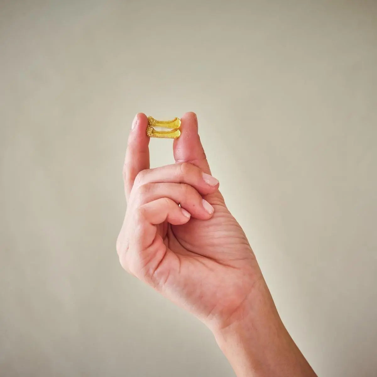 Mano sosteniendo dos cápsulas doradas de Incienso dōTERRA sobre fondo beige