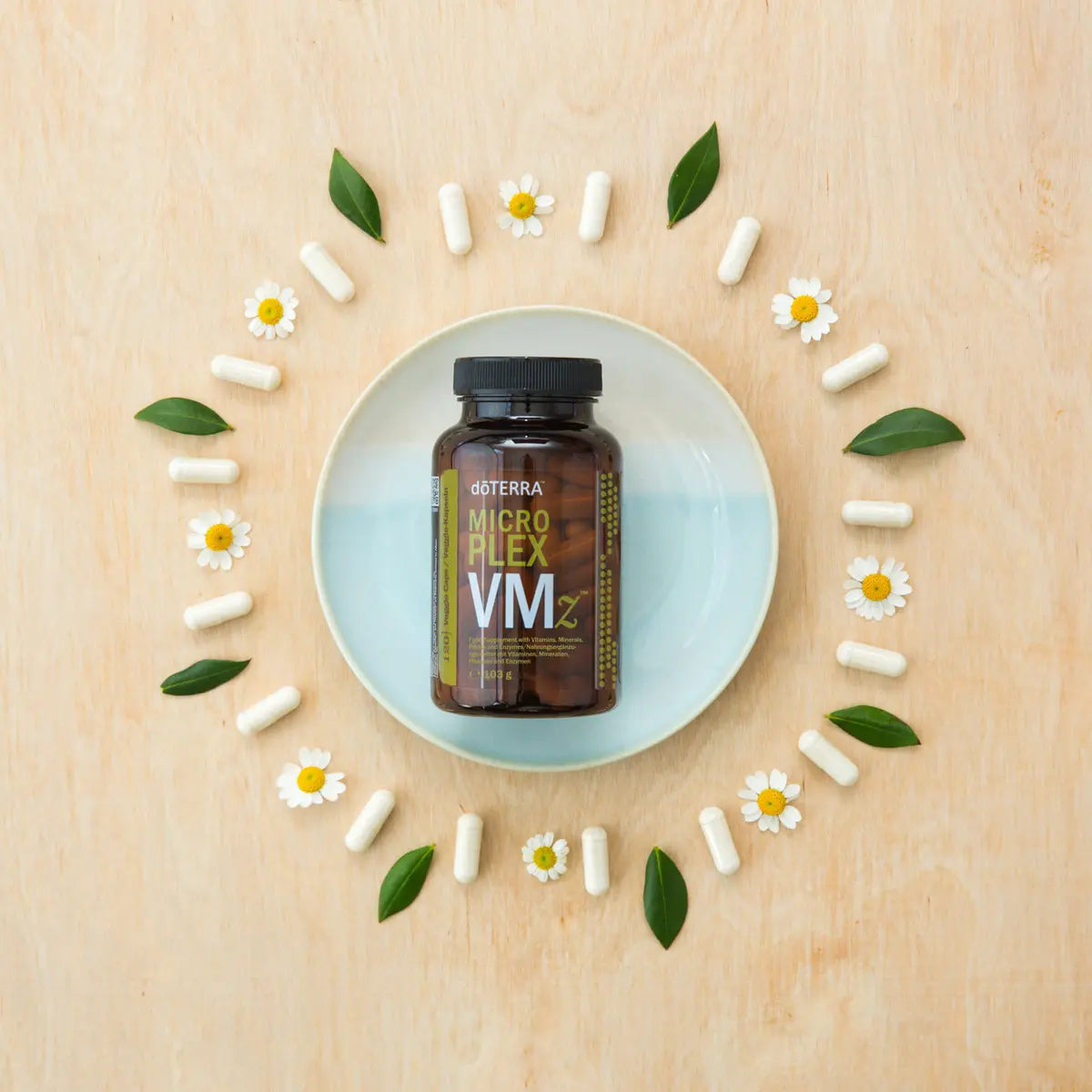 MicroPlex VMz dōTERRA — cápsulas en plato azul con flores en vista cenital