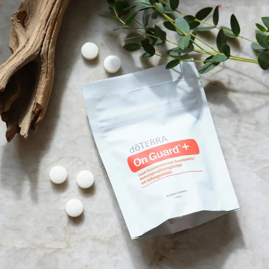 Comprimidos masticables On Guard™+ dōTERRA con bolsa y pastillas sobre mármol con eucalipto, vista cenital