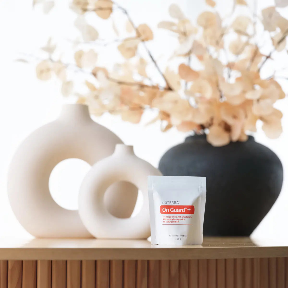 Comprimidos masticables On Guard™+ dōTERRA con bolsa sobre repisa junto a jarrones y flores secas
