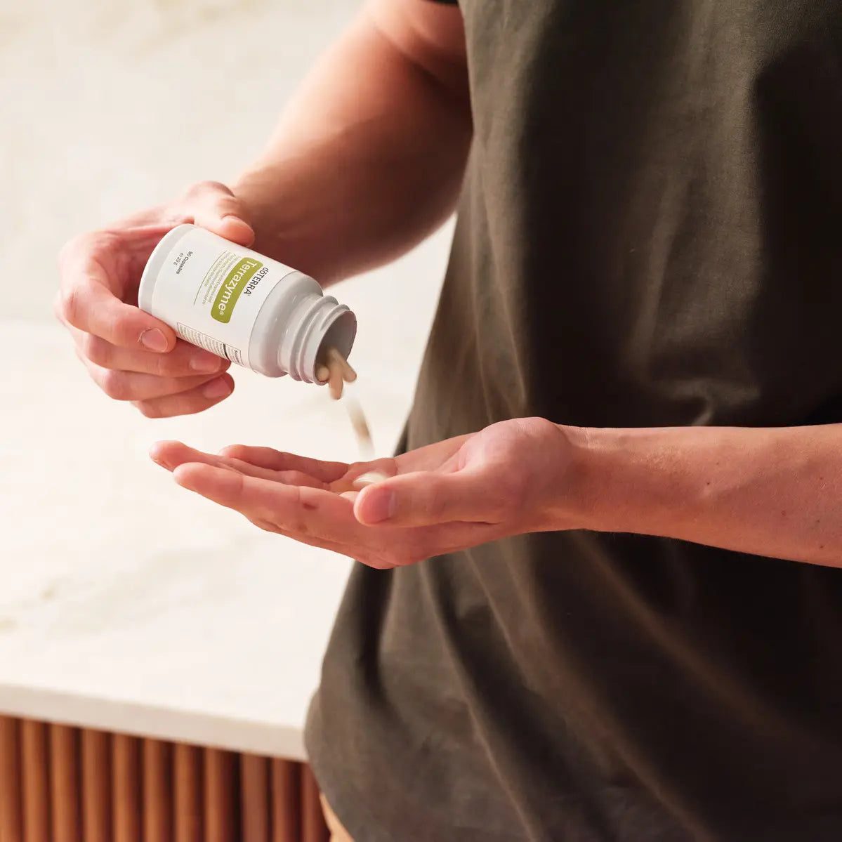 Manos vertiendo cápsula de TerraZyme dōTERRA en la palma en la cocina