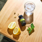Frasco de TriEase dōTERRA 60ct con limón, menta y vaso de hielo sobre madera