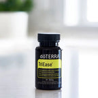 Frasco negro de TriEase Softgels dōTERRA 60ct sobre encimera con planta al fondo