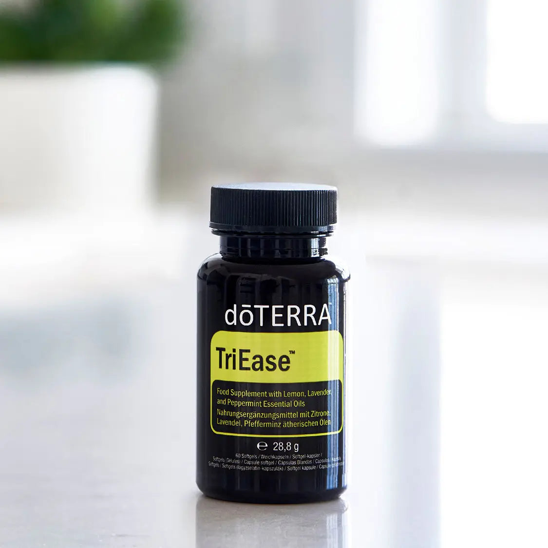 Frasco negro de TriEase Softgels dōTERRA 60ct sobre encimera con planta al fondo