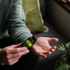 Manos vertiendo softgel de TriEase dōTERRA 60ct en la palma sobre sofá