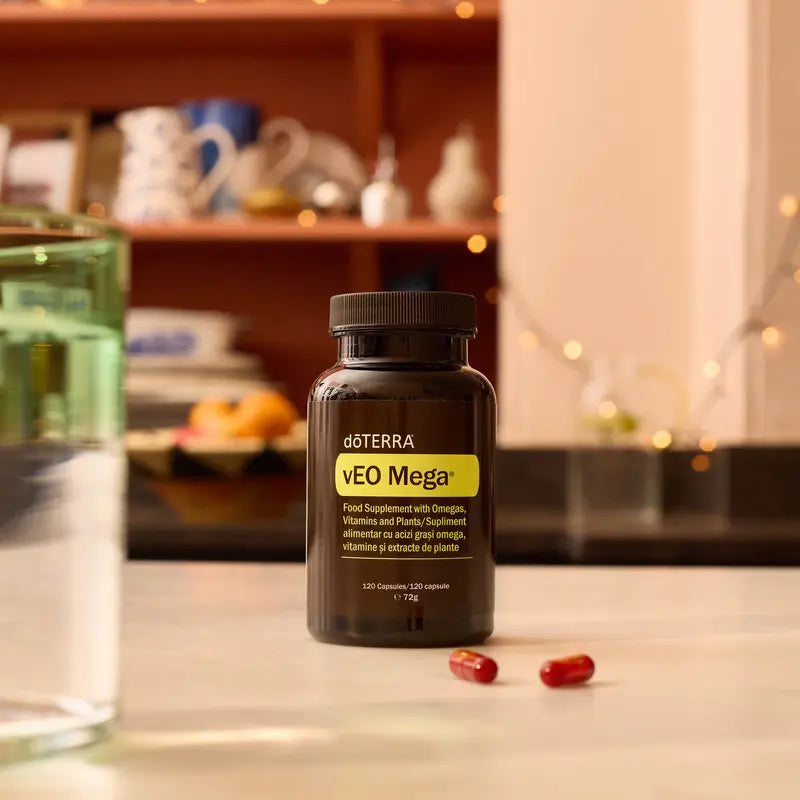 Frasco de suplemento dōTERRA vEO Mega 120 cápsulas sobre encimera de cocina con cápsulas rojas de omega y vaso de agua