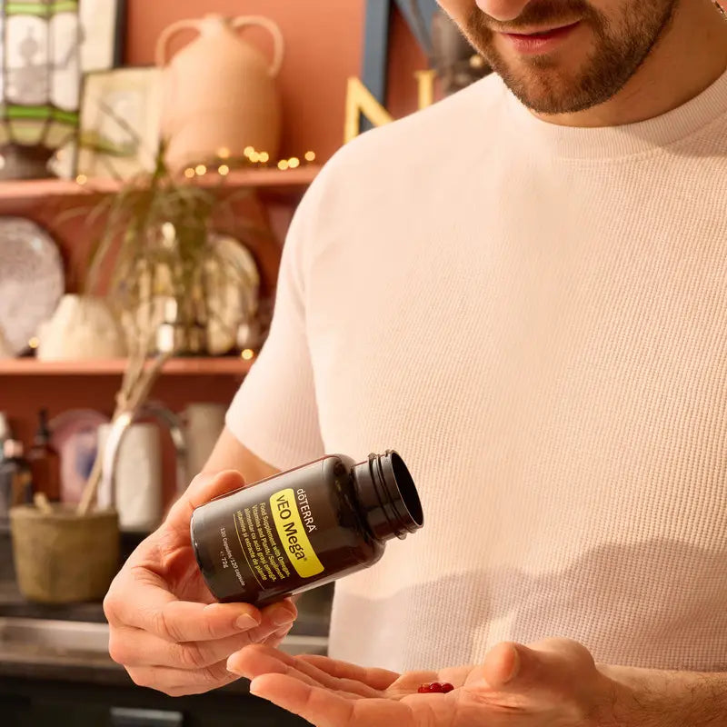 Hombre sosteniendo el frasco de dōTERRA vEO Mega y vertiendo una cápsula roja de omega en la palma de la mano