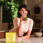 Mujer morena bebiendo batido verde con VMG+ dōTERRA en la cocina