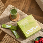 Caja y sobres de VMG+ dōTERRA sobre mesa de madera con batido verde y frutas