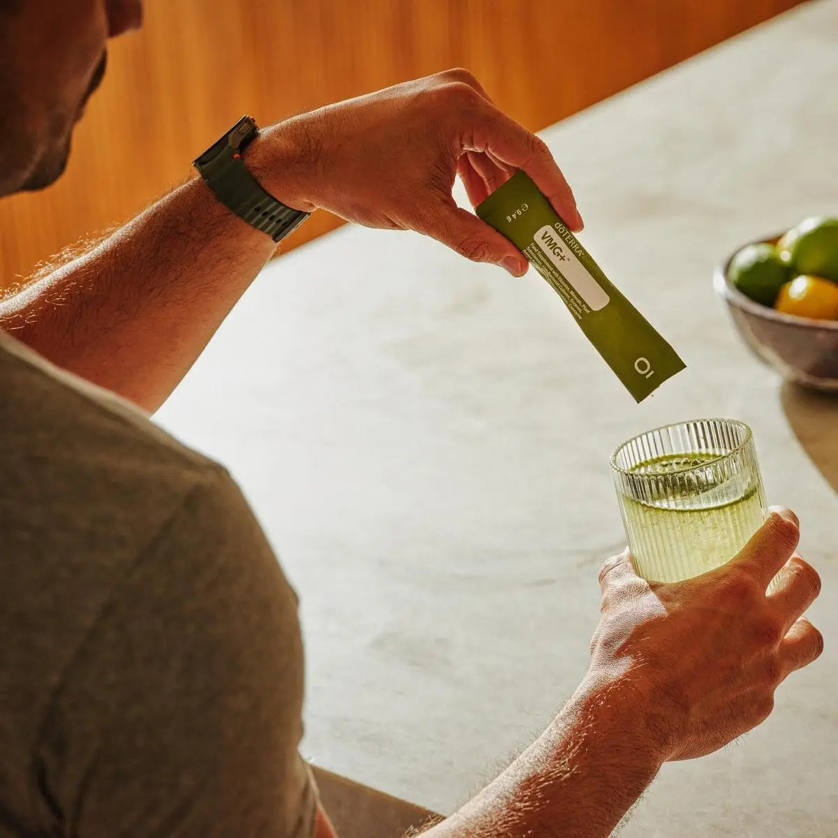 Hombre echando VMG+ dōTERRA en un vaso verde en la cocina