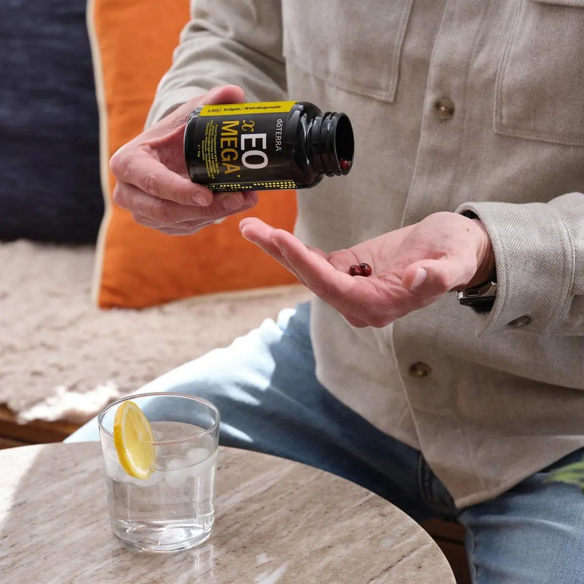 Hombre vertiendo softgels de Xeo Mega dōTERRA 120ct en la palma sobre sofá con limón