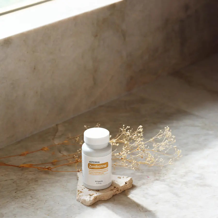 Frasco blanco de Complejo Zendocrine dōTERRA 60ct sobre piedra con ramas secas