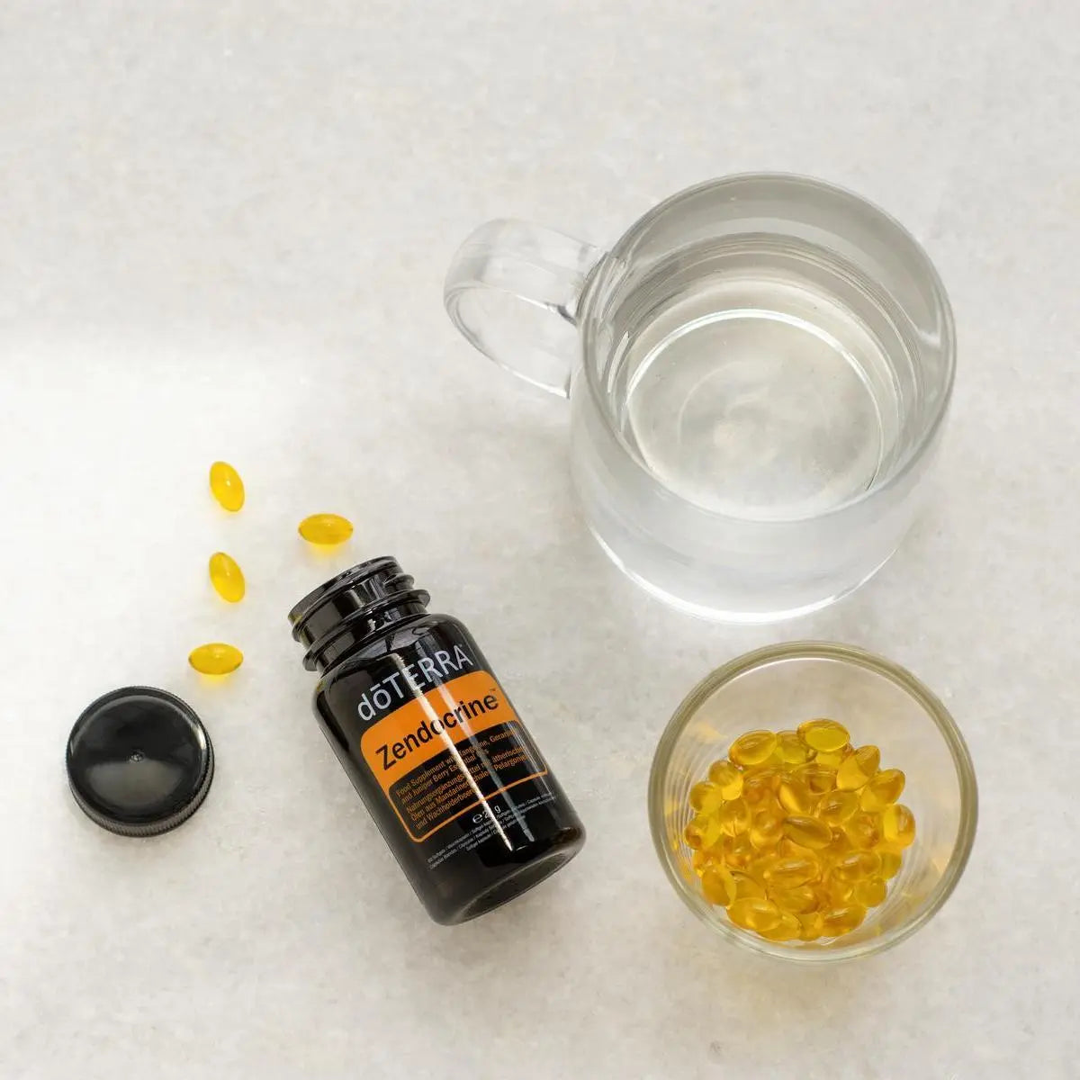 Frasco abierto de Zendocrine Softgels dōTERRA con cuenco de softgels y vaso visto desde arriba
