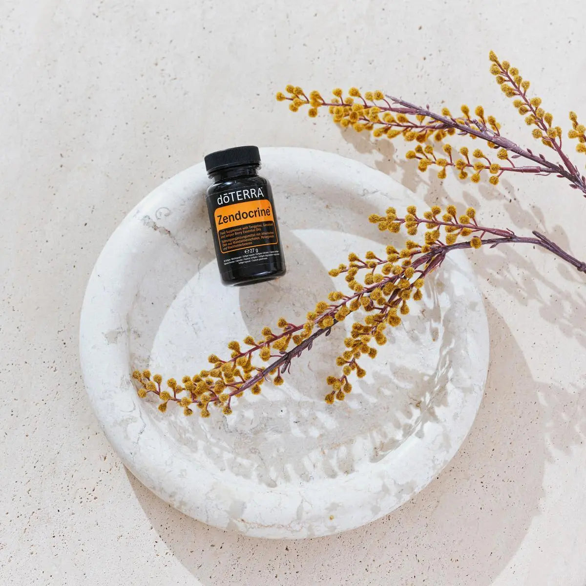Frasco negro de Cápsulas Blandas Zendocrine dōTERRA sobre plato de mármol con ramas secas
