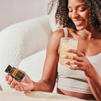 Mujer de cabello rizado con frasco negro de Zendocrine Softgels dōTERRA y vaso en el sofá