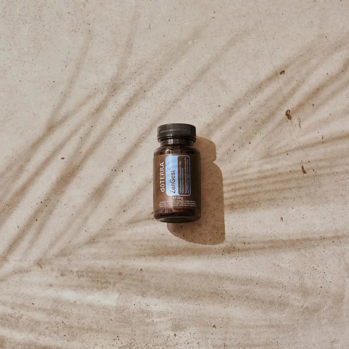 Frasco de Cápsulas ZenGest dōTERRA sobre arena con sombras de palmera visto desde arriba