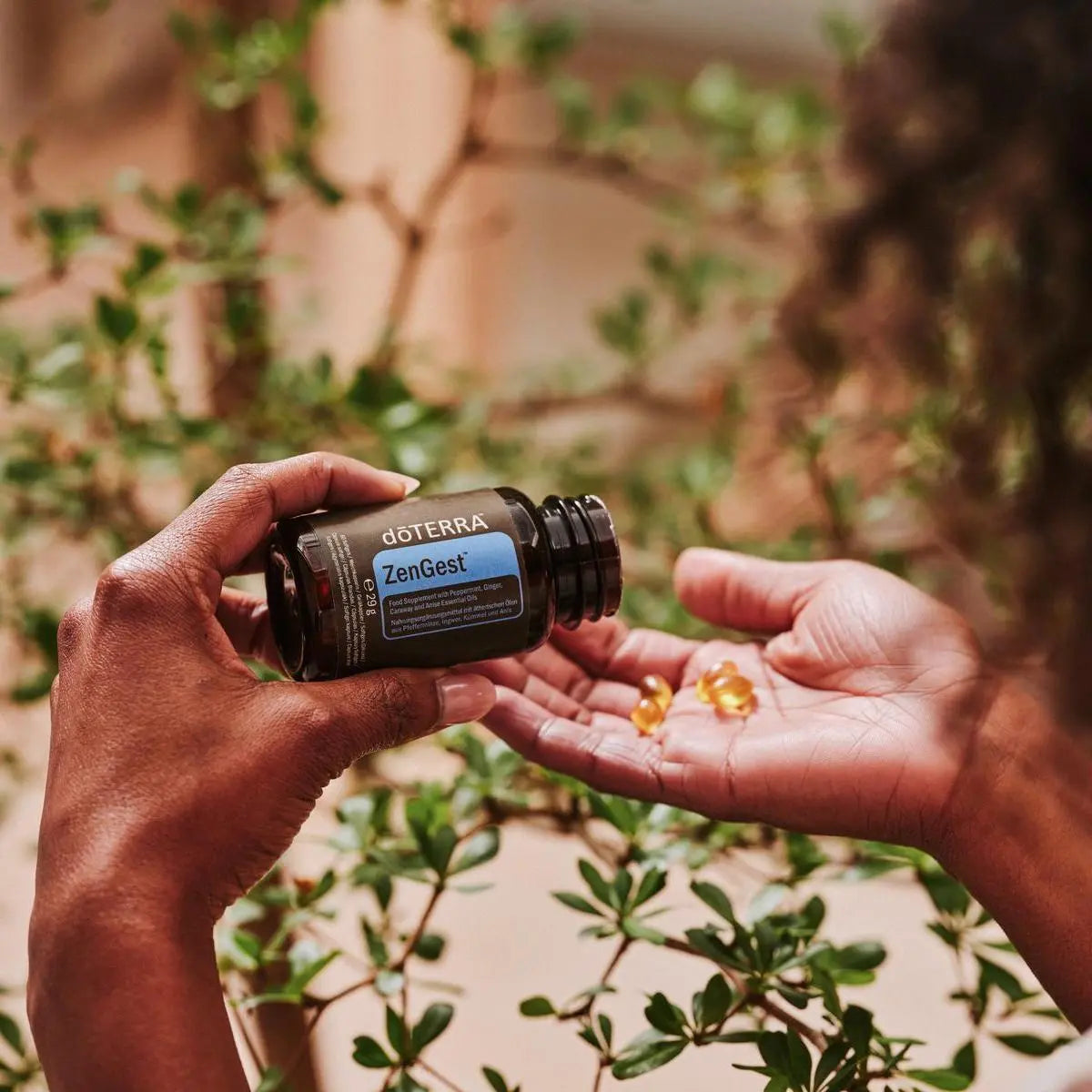 Manos vertiendo softgels de ZenGest dōTERRA en la palma al aire libre