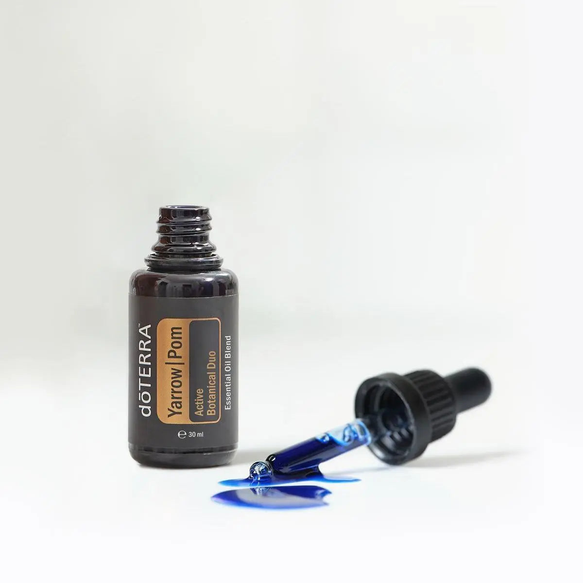 Frasco abierto de Yarrow|Pom dōTERRA 30ml con cuentagotas separado mostrando el característico aceite de color azul índigo derramado sobre superficie blanca