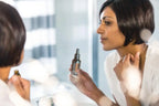 Mujer con cabello negro corto en albornoz blanco sosteniendo el Yarrow|Pom dōTERRA 30ml frente al espejo del baño mientras se toca el cuello